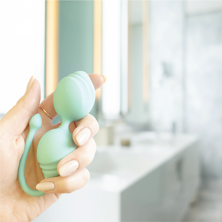 Hand holding the mint green TensCare Fleur pelvic exerciser in a bathroom