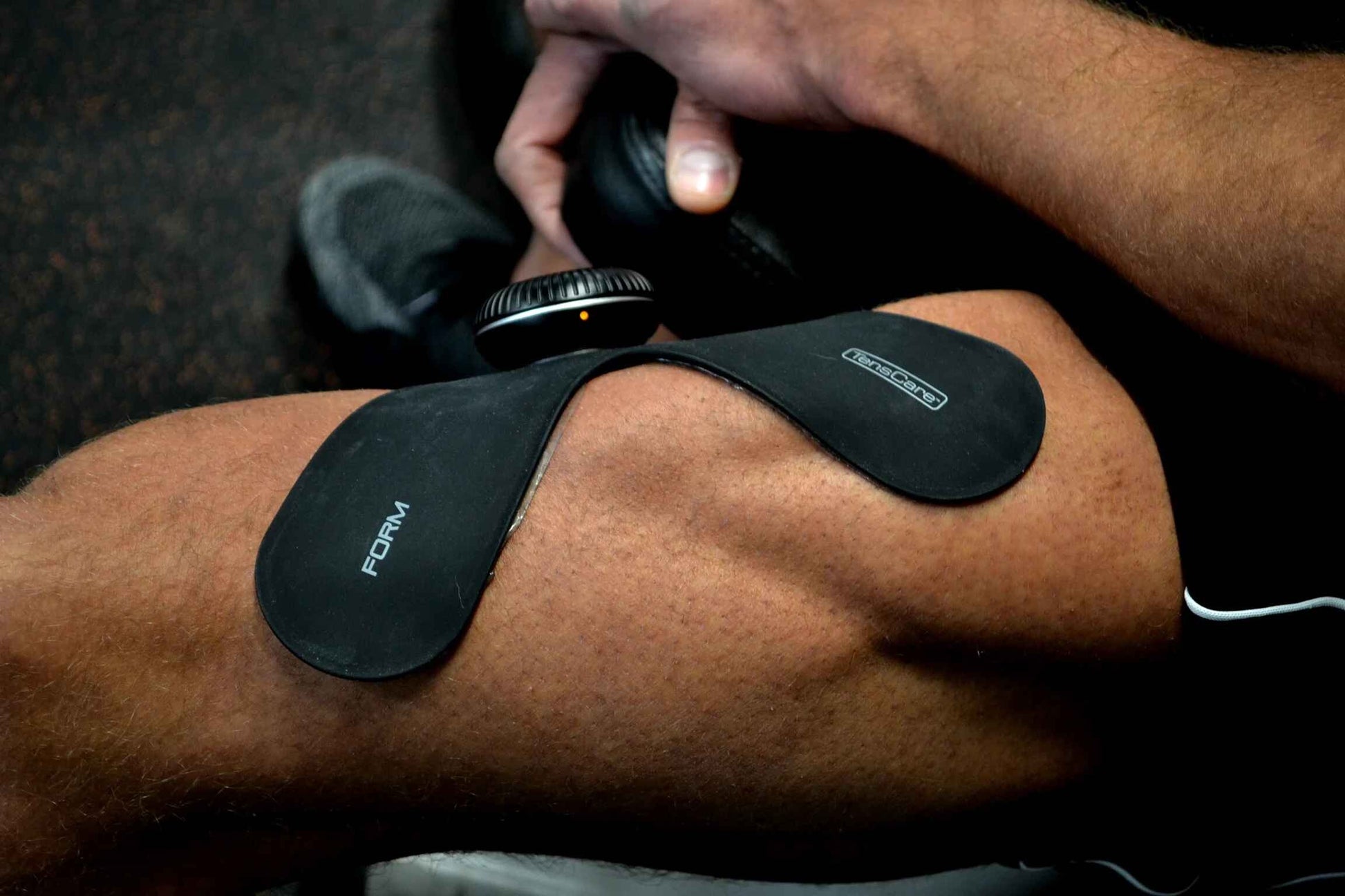 FORM electrode pads applied to a thigh, with a hand pressing the control pod